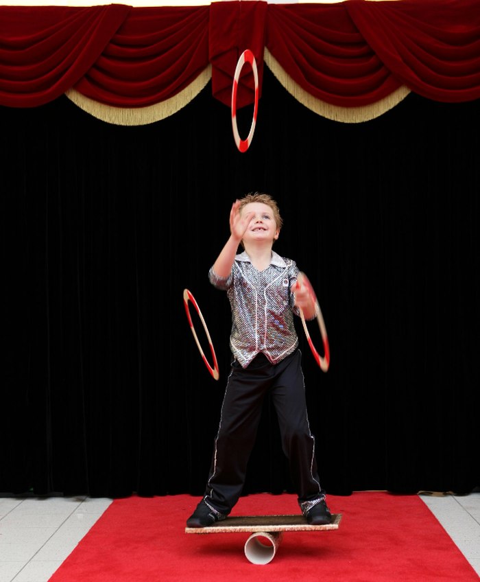 A young Zak Bowdler juggling rings while balancing on a rola bola